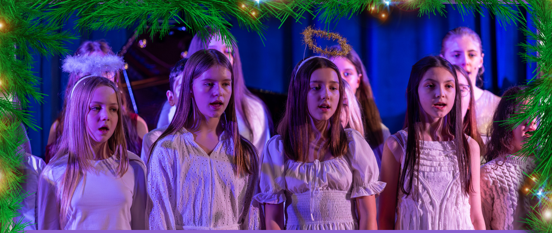 Kilkuosobowa grupka ubranych na biało dzieci podczas występu na scenie, za nimi niebieskie tło, wokół obrazka świąteczna ramka