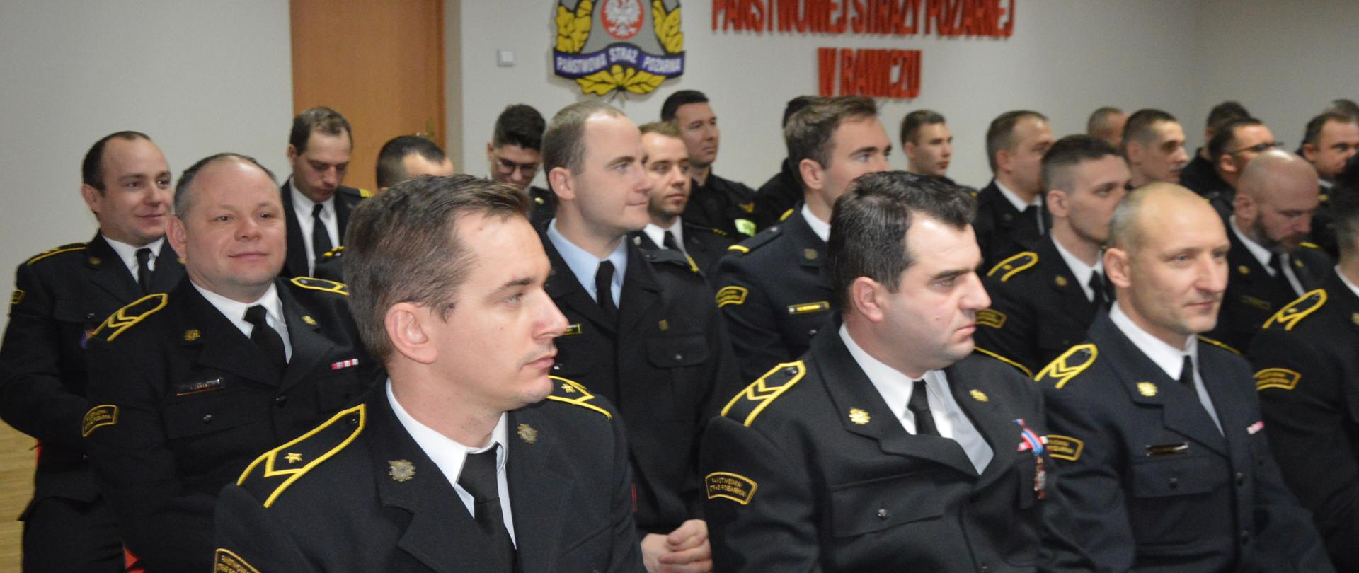 Narada roczna W świetlicy komendy powiatowej PSP w Rawiczu siedzą uczestnicy narady - funkcjonariusze komendy. Strażacy występują w umundurowaniu wyjściowym i koszarowym. W tle ściana, na której widnieje napis w kolorze czerwonym "Komenda Powiatowa Państwowej Straży Pożarnej w Rawiczu" oraz logo PSP.