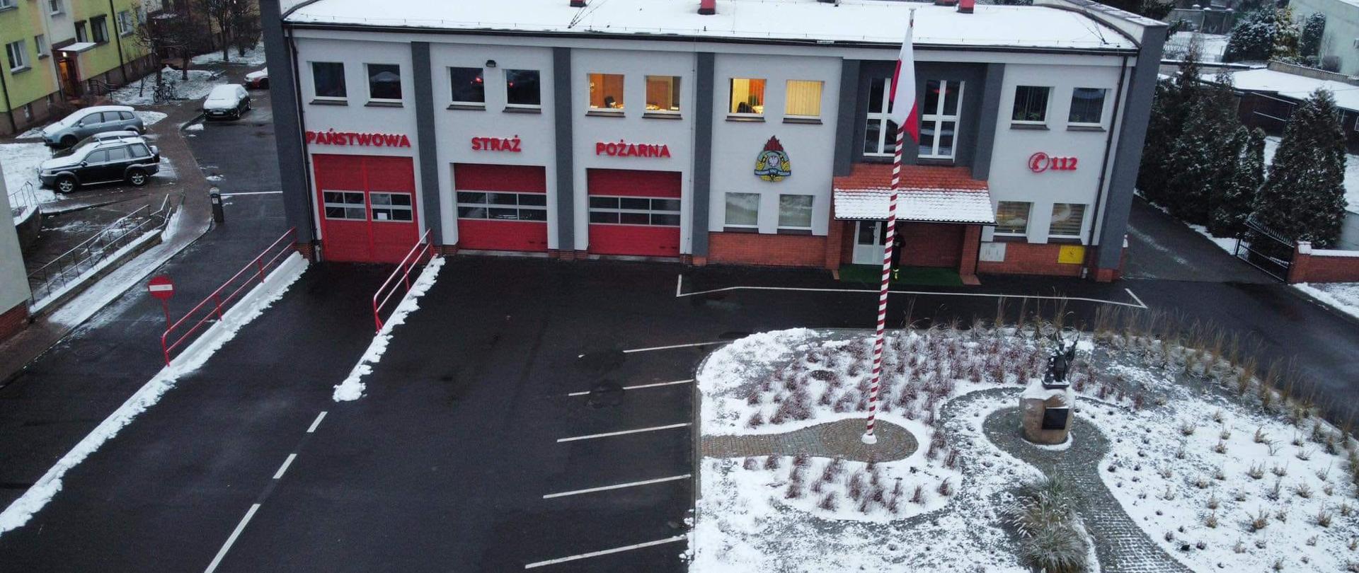 Zdjęcie przedstawia widok z góry budynku komendy powiatowej PSP w Krotoszynie oraz teren zewnętrzny po nasadzeniu roślinności. Na elewacji budynku napis Państwowa Straż Pożarna, logo PSP i numer alarmowy 112. 