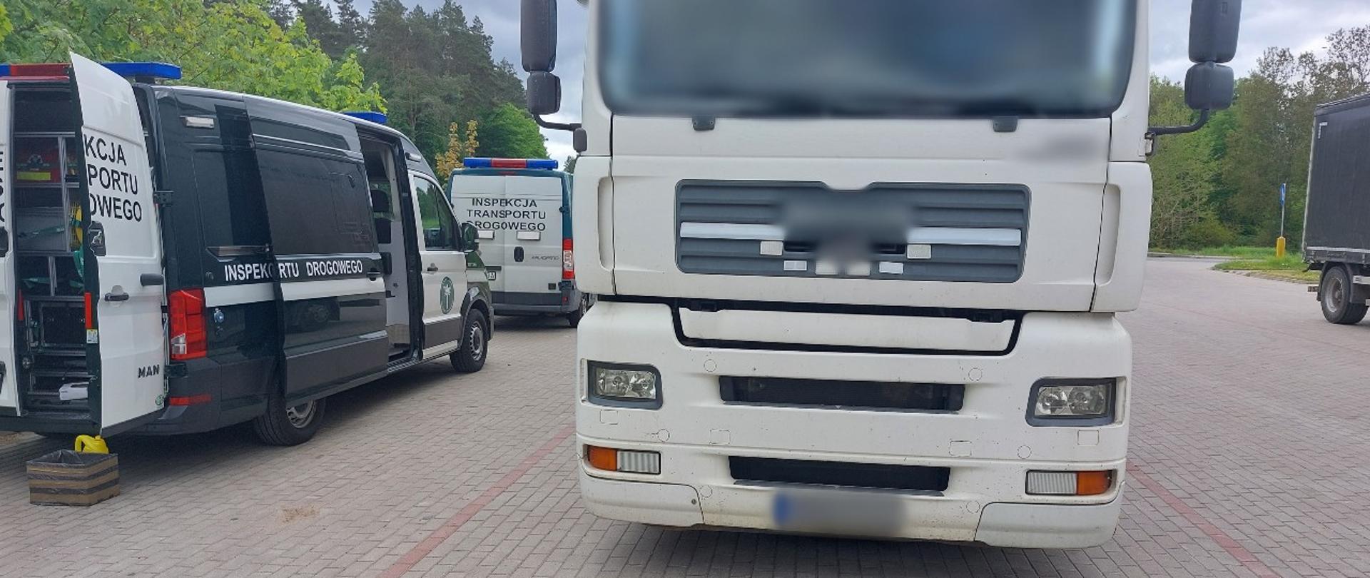 Od lewej: tył i prawy bok dwóch oznakowanych furgonów warmińsko-mazurskiej Inspekcji Transportu Drogowego. Obok stoi kontrolowany samochód ciężarowy.