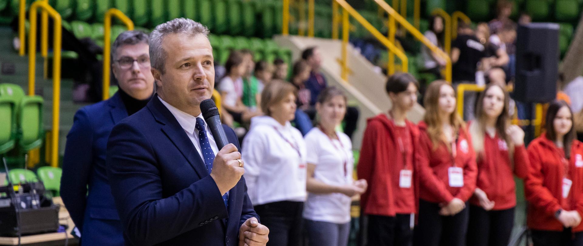 Jeden mężczyzna stojący z mikrofonem i wypowiadający się 