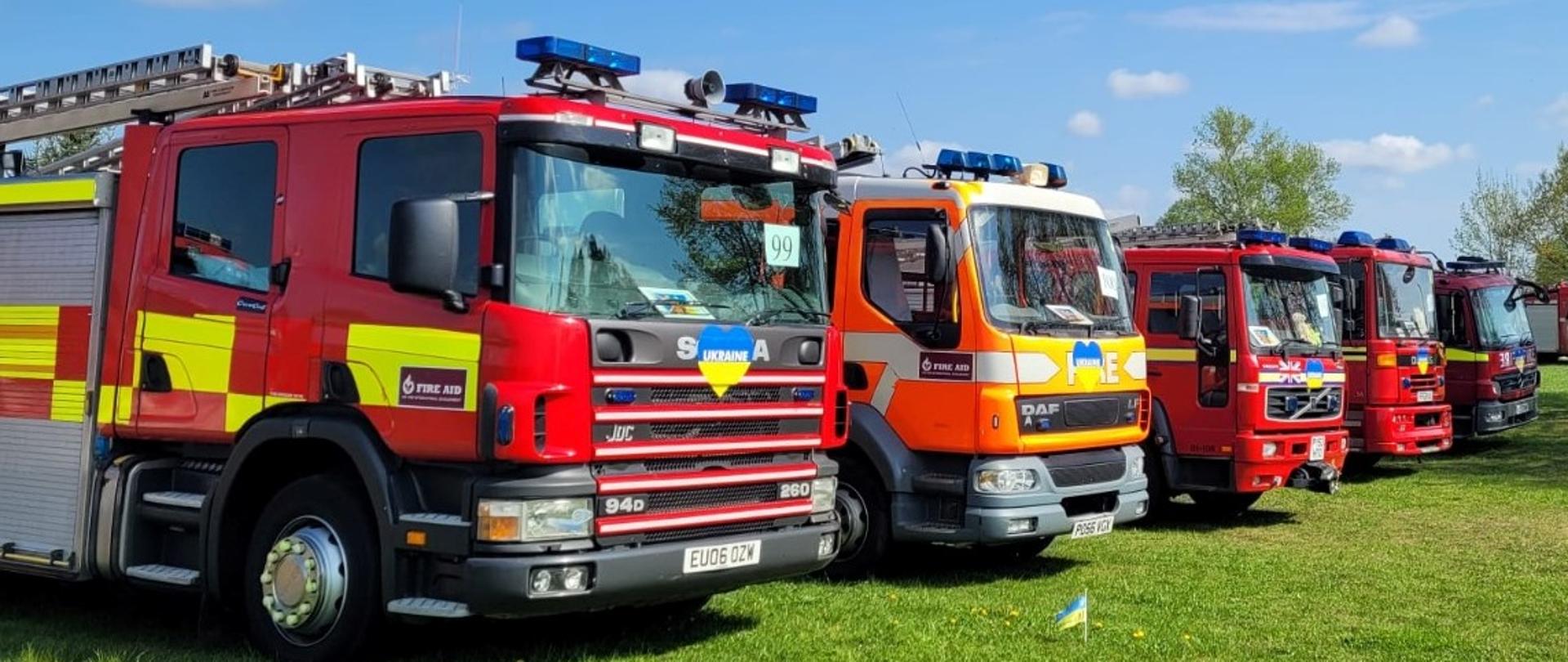 Na zdjęciu widać pięć samochodów straży pożarnej stojących na podłożu trawiastym.