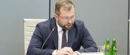 Minister Grzegorz Puda na posiedzeniu Komitetu Koordynującego ds. Polityki Rozwoju, minister siedzi przy stole i przemawia do mikrofonu