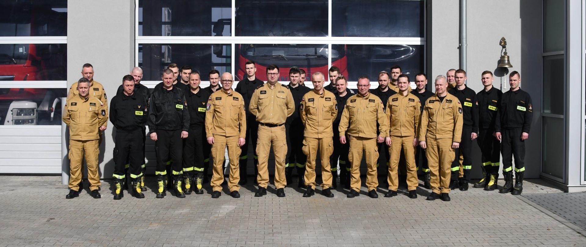 Zdjęcie grupowe kursantów przed bramą wyjazdową JRG Śrem, na zdjęciu funkcjonariusze w nowych ubraniach służbowych koloru żółtego oraz w czarnych ubraniach koszarowych