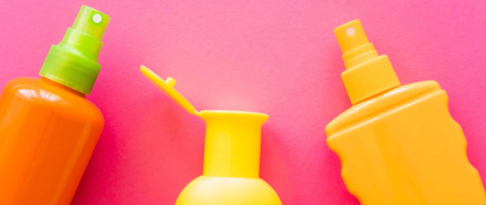 Na zdjęciu są trzy butelki kremów. Znajdują się na różowym tle.