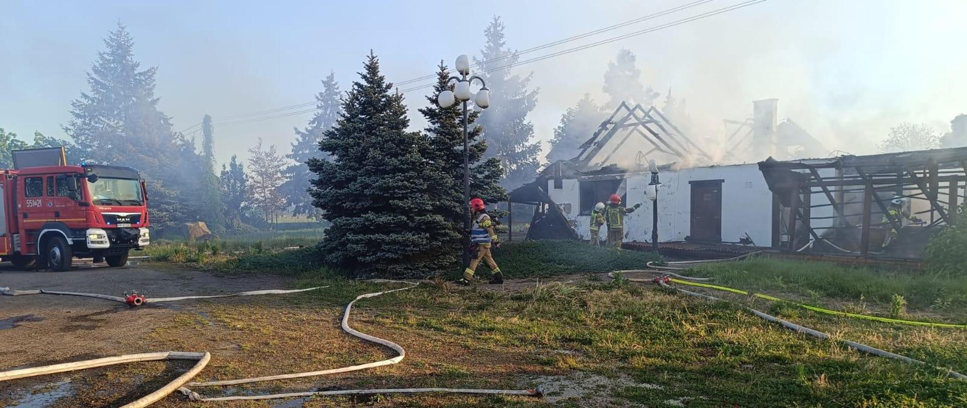 Strażacy podczas dogaszania pożaru w tle wóz strażacki.