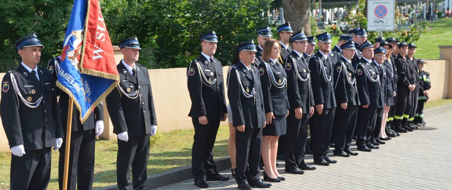 Poczet sztandarowy OSP Chmielno, za którym w dwuszeregu ustawieni są członkowie OSP.