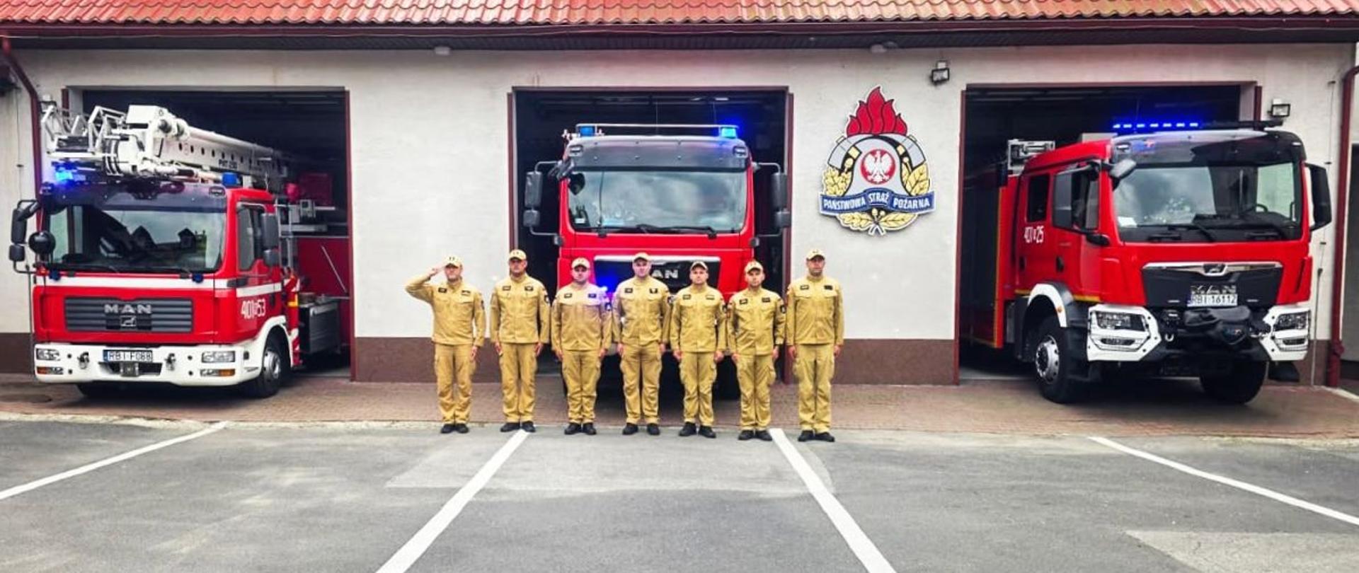 Zdjęcie przedstawia zmianę służbową przed garażami JRG. Samochody są na zewnątrz z włączonymi światłami błyskowymi. Dowódca oddaje honor, reszta stoi na baczność.