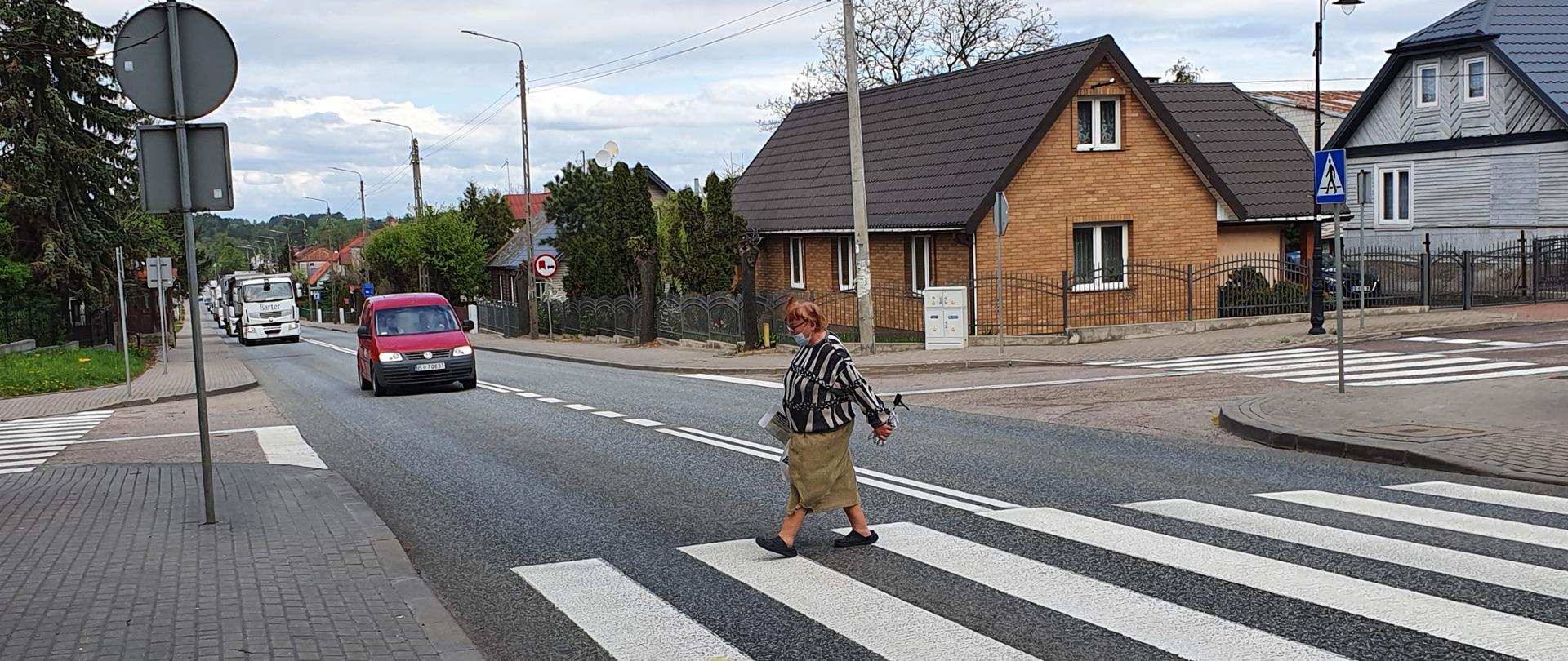Auta zwalniają przed starszą kobieta przechodzącą przez przejście 