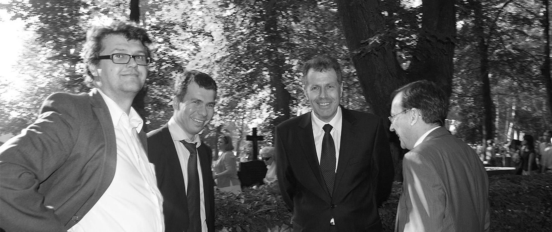 Na czarno-białym zdjęciu widać m.in. ministra Mariusza Kamińskiego i wiceministra Macieja Wąsika stojących ze śp. Władysławem Stasiakiem. W tle widać cmentarne krzyże.