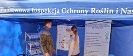 Mężczyzna stojący wewnątrz stoiska WIORiN w formie niebieskiego namiotu wystawowego. Obok kierownik Oddziału pokazująca na tablicy materiały informacyjne.
