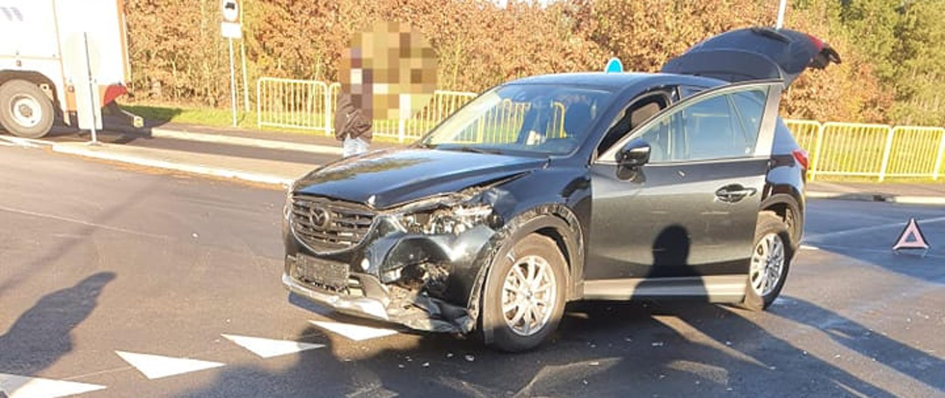 Widać uszkodzony samochód osobowy i leżący skuter na drodze