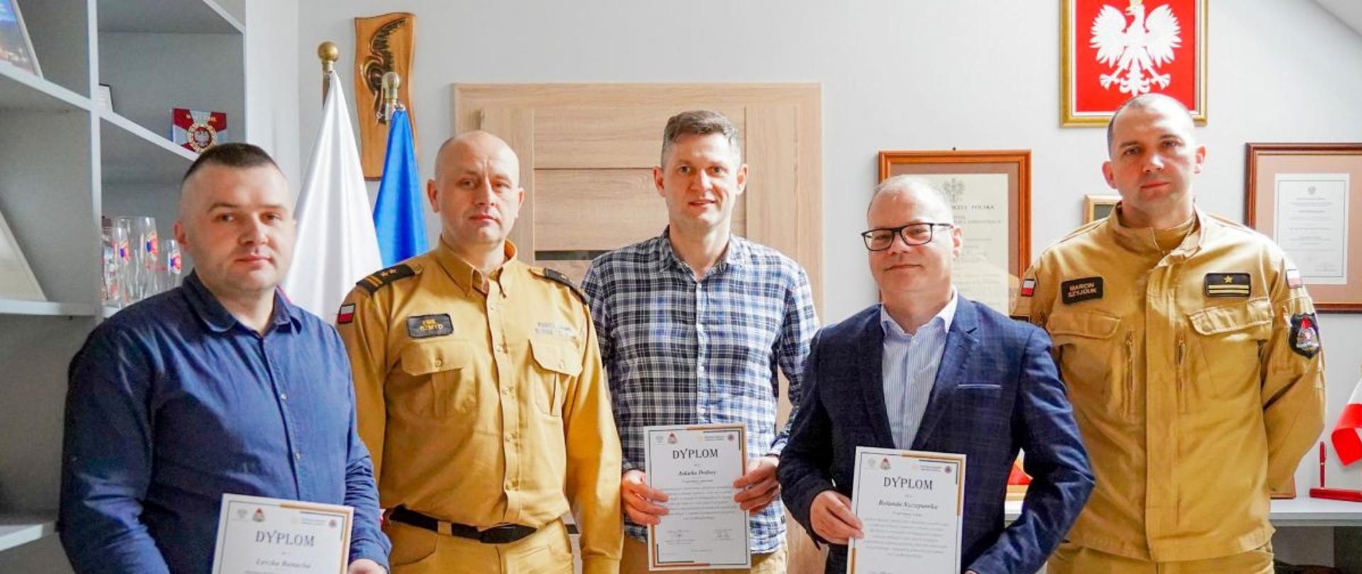 Zdjęcie przedstawia komendanta oraz jego zastępce wraz z trzema przedstawicielami urzędów samorządowych z dyplomami w rękach. 