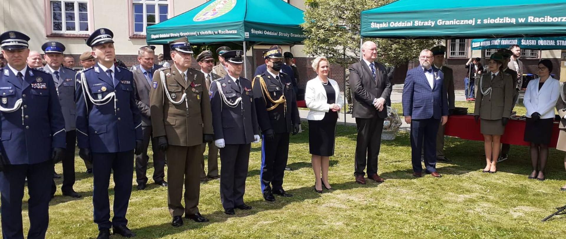 Na zdjęciu - na pierwszym planie, 1 osób, stojących obok siebie na uroczystości w Raciborzu. Od lewej mundurowi, a wśród nich wicewojewoda śląski i wicewojewoda opolski. W tle budynek SG. 