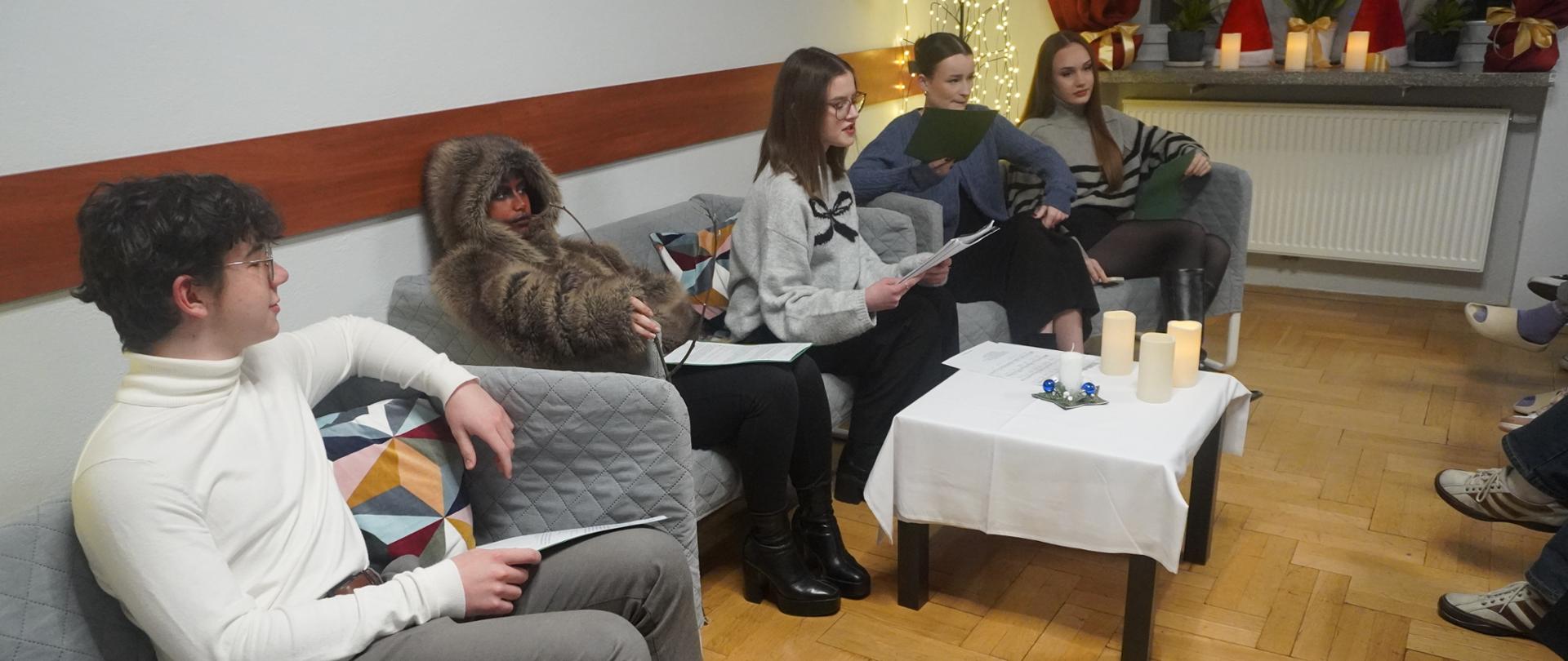 Wychowankowie siedzą na kanapach i przedstawiają zwyczaje wigilijne w Polsce i innych krajach