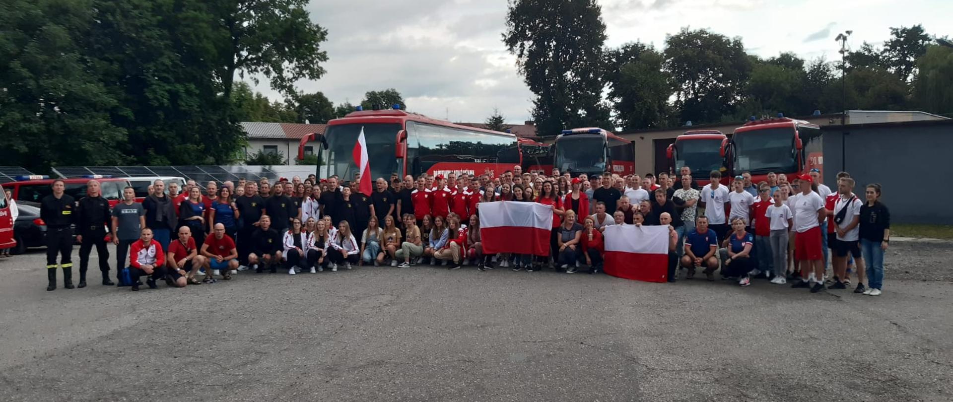 Grupowe zdjęcie polskich reprezentantów wybierających się na zawody CTIF 2022. W tle widoczne autokary oraz busy