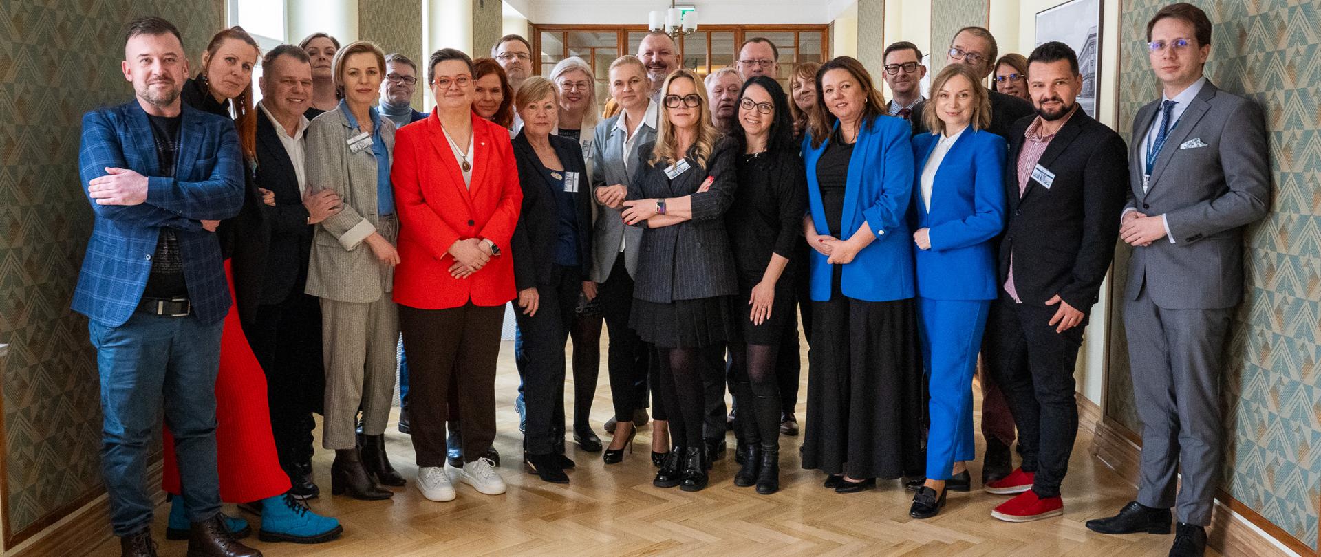 Spotkanie ministrów z Nauczycielami Roku. Zdjęcie grupowe przedstawia wszystkich nauczycieli roku i wiceministrów. Wszyscy stoją na korytarzu w MEN