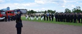 Apel z okazji obchodów Dnia Strażaka, w tle pododdział strażaków ubranych w ciemnogranatowe mundury wyjściowe, a także orkiestra.