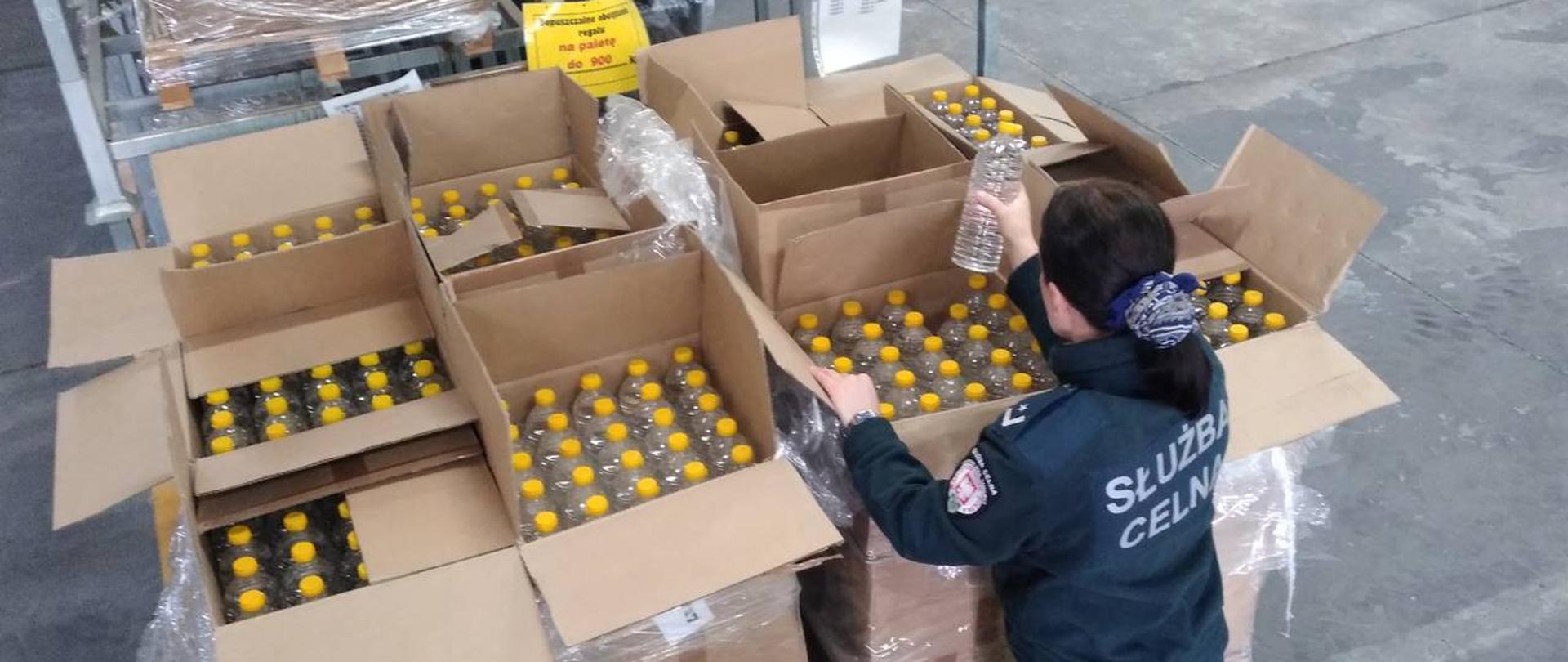 Funkcjonariuszka KAS przy pudłach z butelkami z alkoholem.