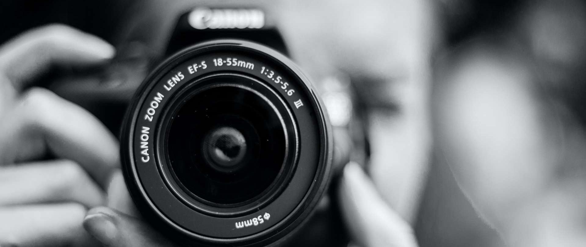 zdjęcie obiektywu z osobą fotografującą na drugim planie