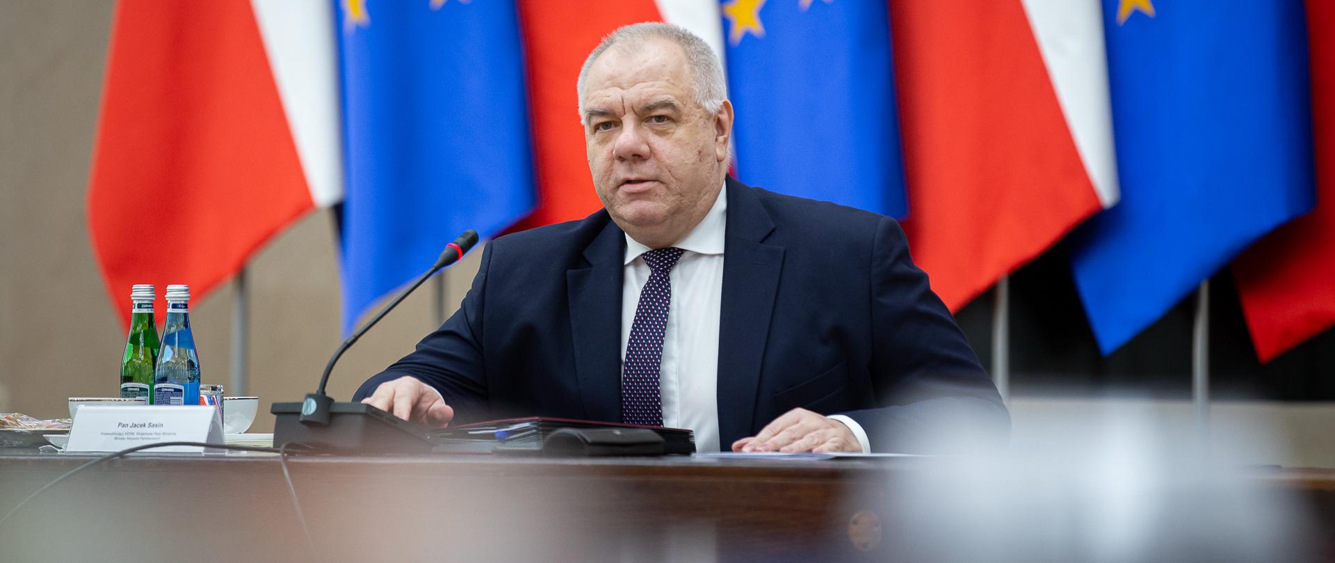 Wicepremier Jacek Sasin, bliski plan. W tle flagi - polskie i unijne. 