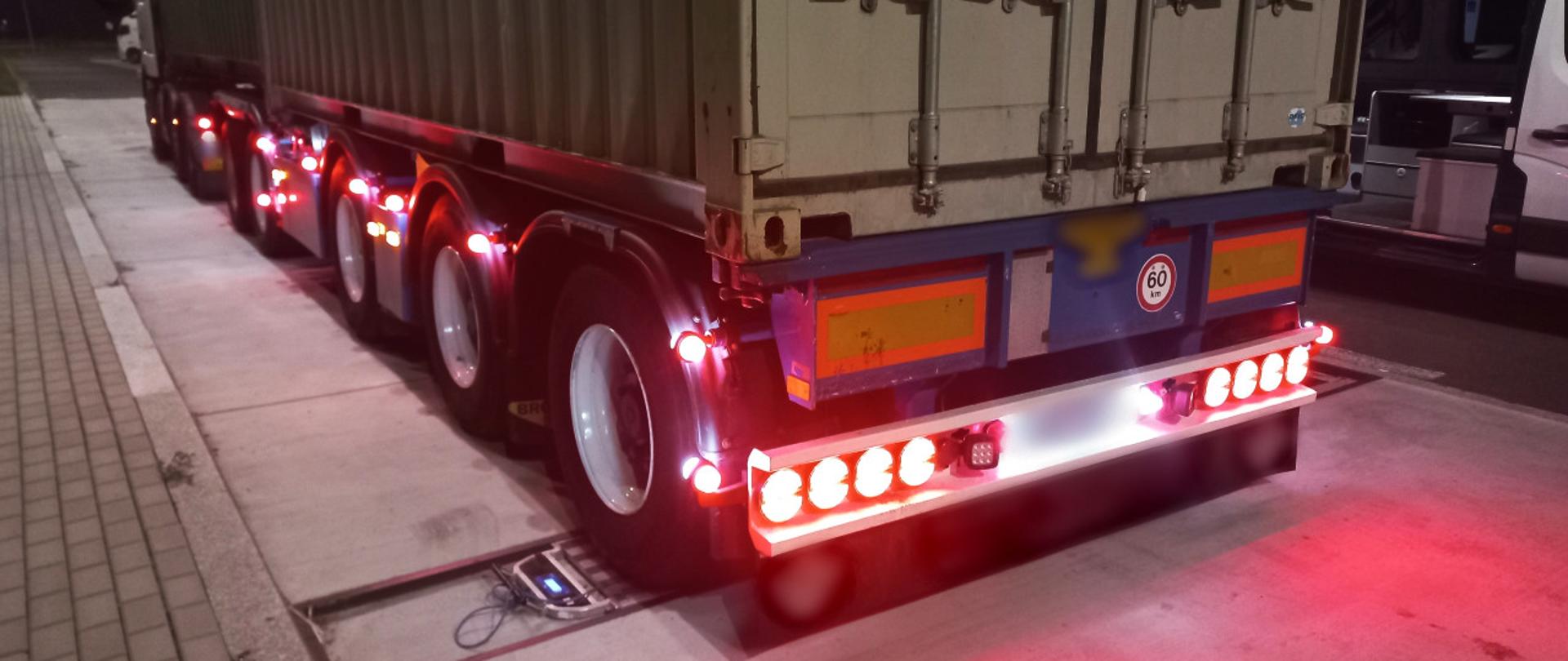 Od lewej: ciągnik siodłowy z podpiętą naczepą dzieloną, przewożący dwa kontenery z ładunkiem, przejeżdża przez inspekcyjne wagi. Obok kontrolowanego zestawu stoi oznakowany furgon mazowieckiej Inspekcji Transportu Drogowego z otwartymi drzwiami do przestrzeni kontrolno - biurowej.