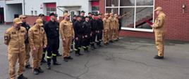 Funkcjonariusze stoją na placu komendy w dwuszeregu. Przed nimi stoi komendant.