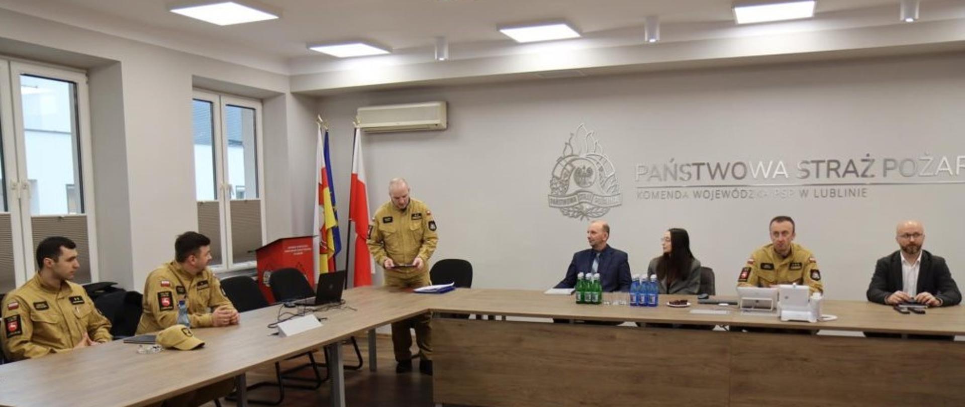 Na sali narad Komendy Wojewódzkiej PSP siedzą trzy osoby z PGW Wody Polskie RZGW w Lublinie oraz trzech przedstawicieli PSP w Lublinie. Jeden z pracowników PSP stoi i trzyma w dłoniach tekst.