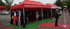 Zdjęcie przedstawia komendanta miejskiego PSP st. bryg. Bogusława Szczurko podczas przemówienia, w tle pod czerwonym zadaszeniem zaproszeni goście