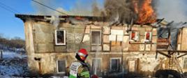 Strażacy PSP gaszą pożar budynku mieszkalnego objętego ogniem, z którego wydobywają się płomienie i gęsty dym.