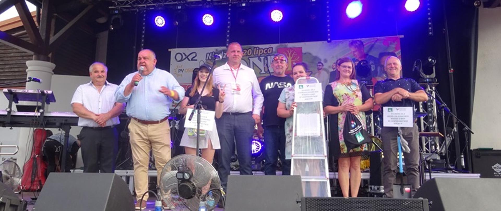 Na scenie od lewej stoją; Krzysztof Bartusiak – Kierownik DPO PT KRUS w Jaśle, Jan Urban – Dyrektor OR KRUS w Rzeszowie, Marek Rączka – Wójt Gminy Osiek Jasielski oraz laureaci w konkursie, który trzymają w rękach nagrody oraz upominki