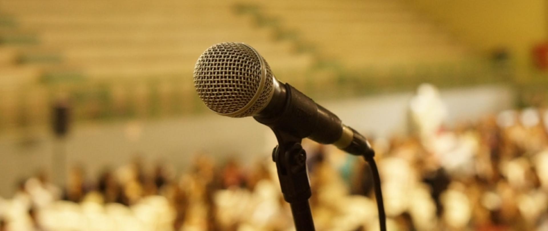 Mikrofon na statywie na tle rozmytego audytorium z publicznością.