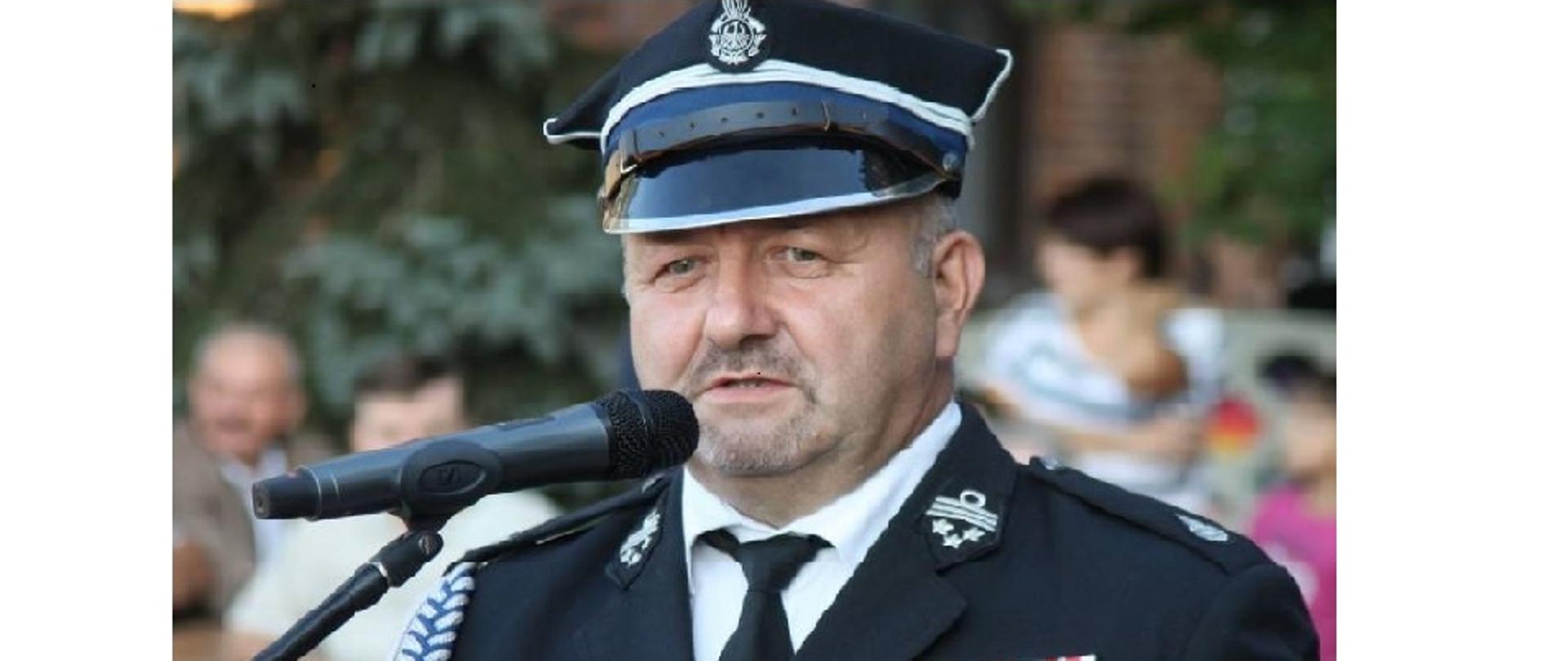 Wizerunek druha Waldemara Florkowskiego w mundurze wyjściowym formacji osp. Druh przemawia przed mikrofonem. W tle widać duzą ilość ludzi