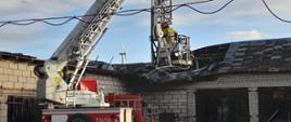 Zerwany dach budynku gospodarczego a przed nim podnośnik strażacki, w którego koszu jest strażak.