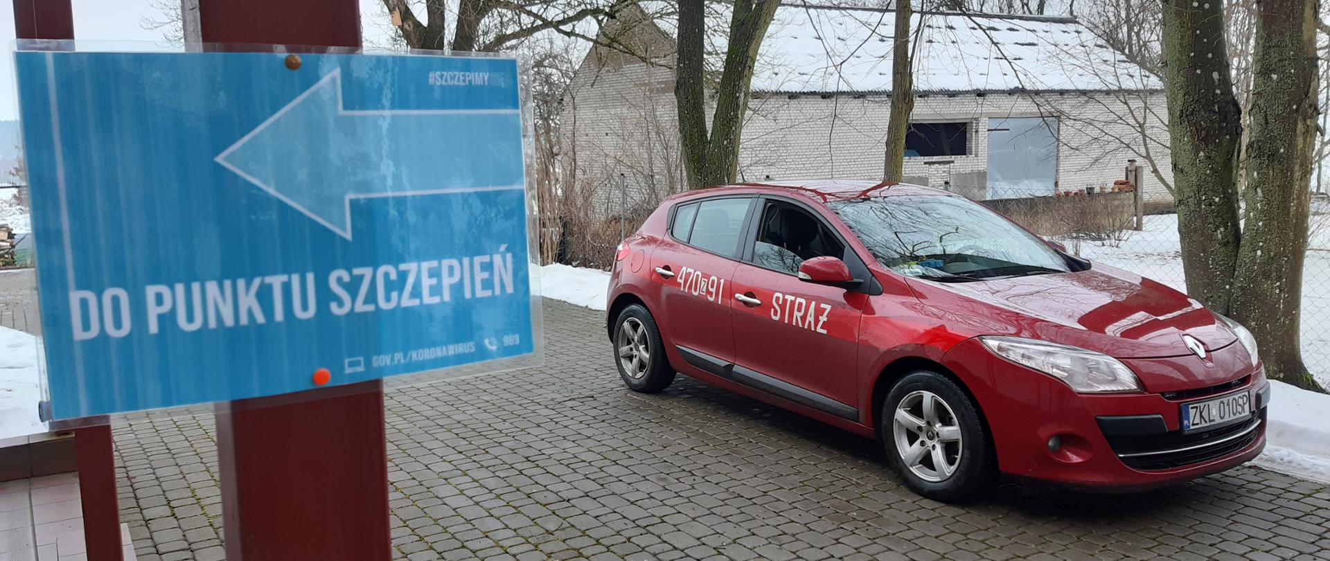Czerwony samochód, na drzwiach napis "Straż" oraz numer 470Z91. Na słupie kartka ze strzałką i napisem "Do punktu szczepień"