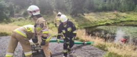 Zdjęcie przedstawia strażaków podczas ćwiczeń znajdujących się przy punkcie czerpania wody ze zbiornika naturalnego. 