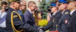 Wojewoda podaje rękę strażakom stojącym w rządku