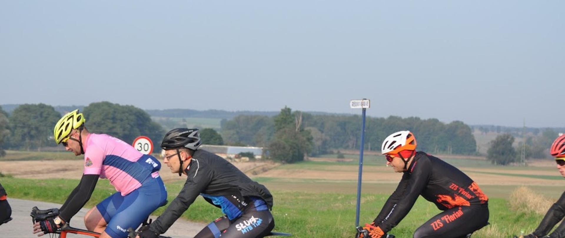 Zdjęcie przedstawia rowerzystów uczestniczących w IV edycja 500 + km na rowerze. Wszyscy poruszają się na rowerach, ubrani w stroje sportowe.