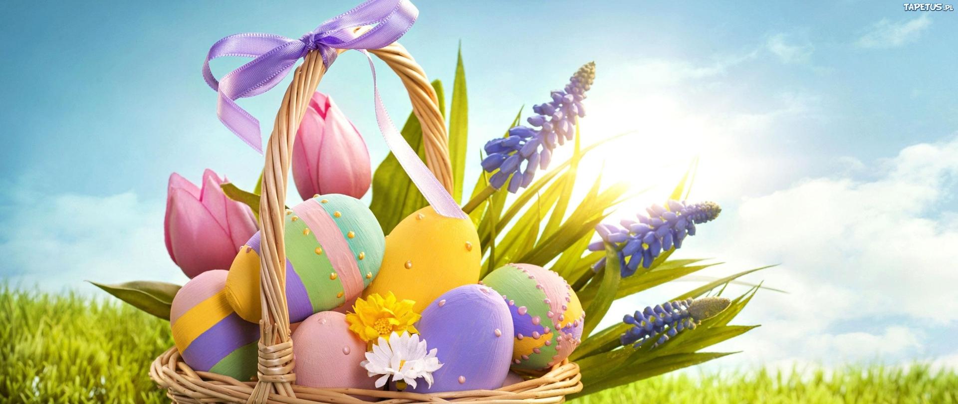 Koszyk wiklinowy znajdujący się na zielonej łące, wewnątrz koszyka pisanki