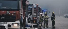 Zdjęcie przedstawia wozy bojowe i strażaków podających wodę do pożaru