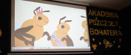 Zdjęcie ściany, na czarnym tle żółty napis Akademia Pszczoły Bohatera i obrazek dwóch pszczół, jedna w koronie.