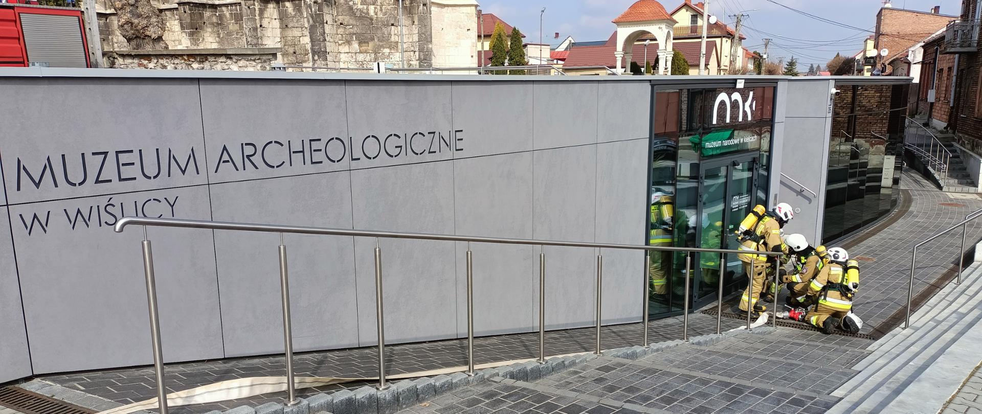 budynek muzeum, na dole strażacy w ubraniach bojowych i rozwijają linię główną