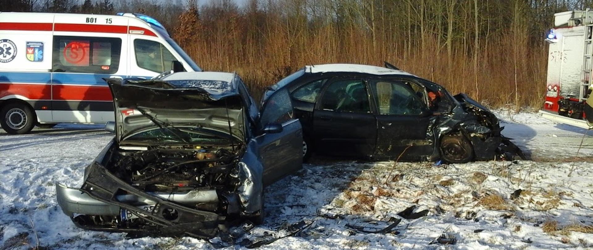 Zdjęcie przedstawia rozbite samochody osobowe na śniegu po uderzeniu czołowym, w tle widać karetkę pogotowia ratunkowego