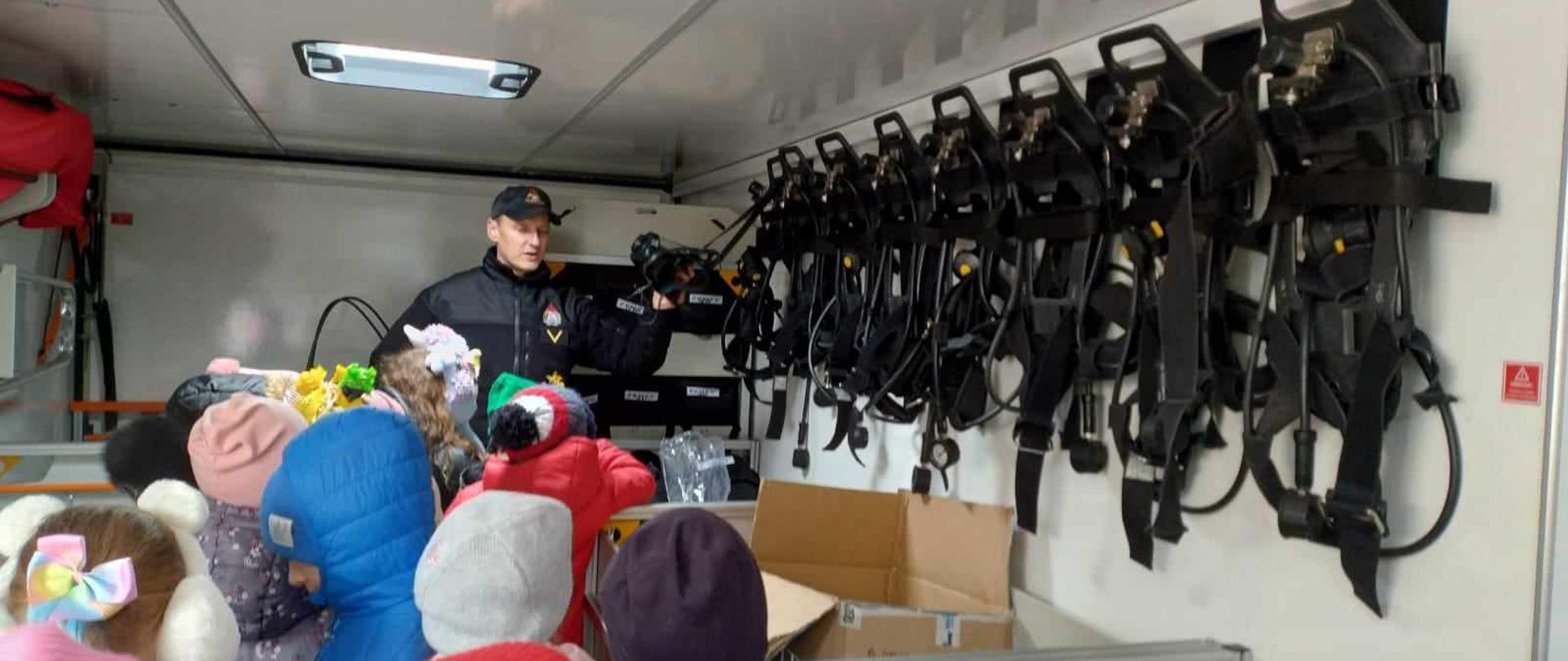 Zdjęcie przedstawia strażaków w trakcie edukacji i pokazów.
W tle samochody strażackie.
