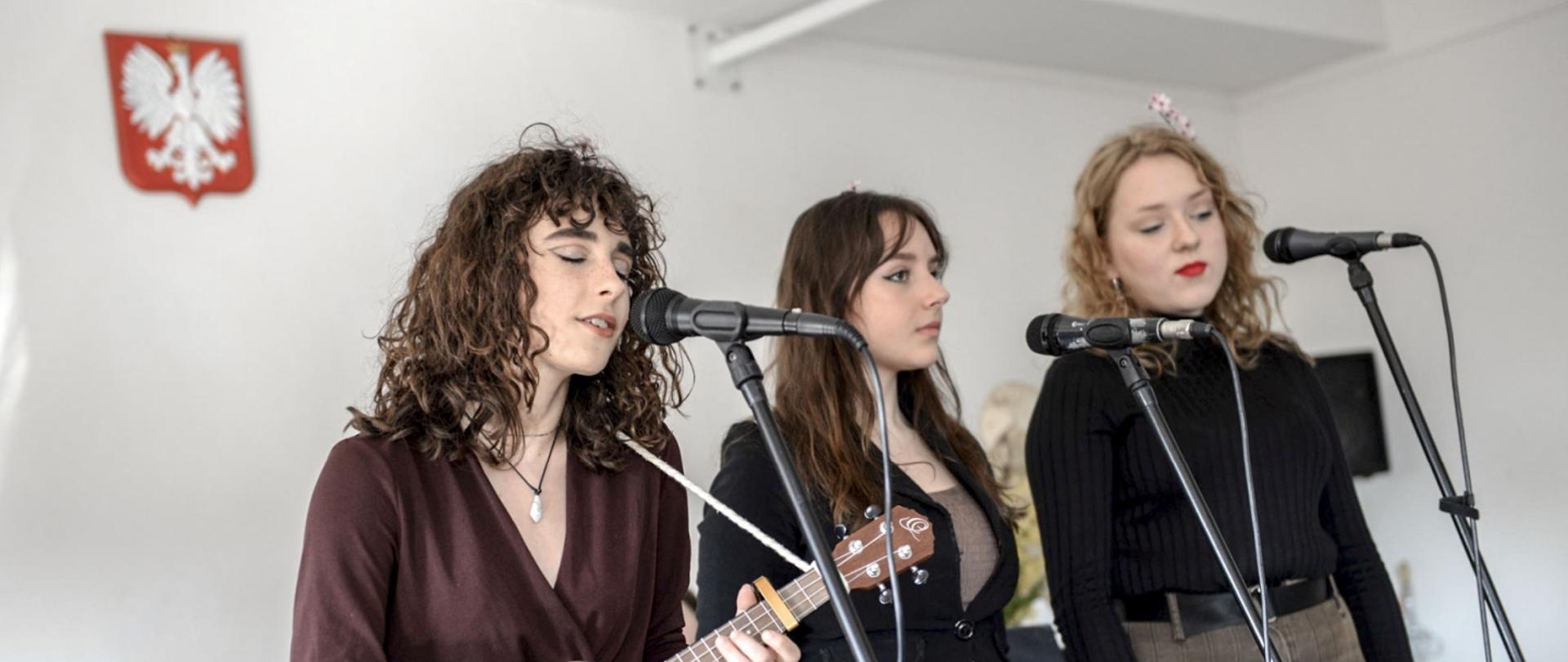 Trzy młode kobiety stoją i śpiewają na scenie