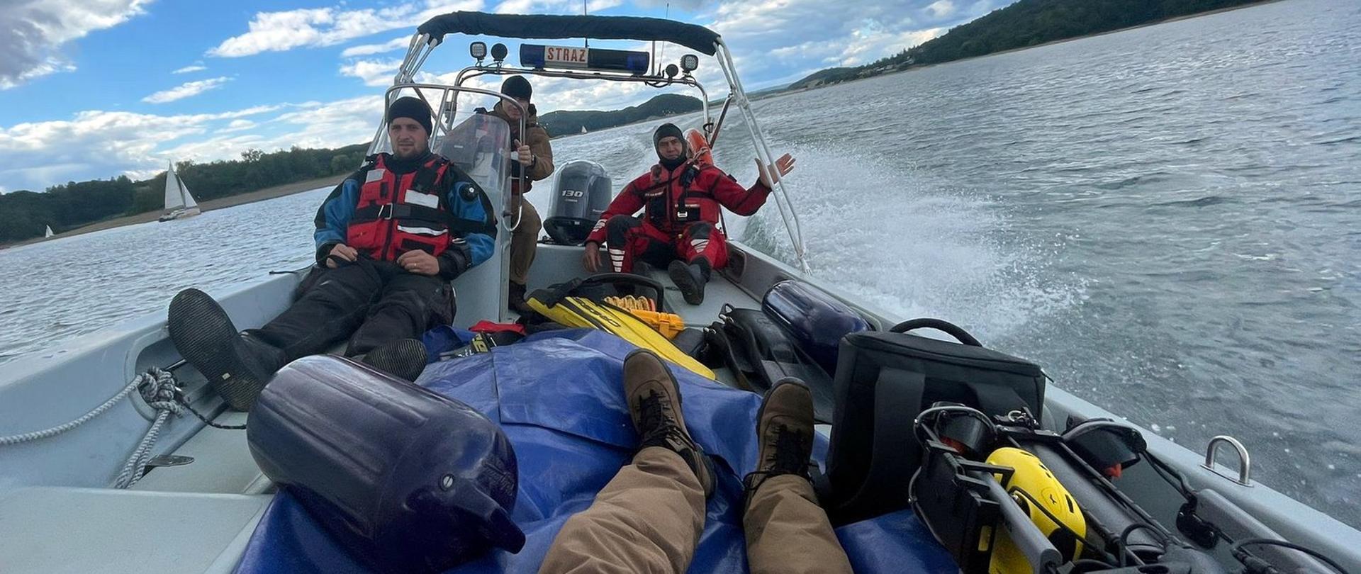 Zdjęcie wykonane na zewnątrz, na jeziorze. Wnętrze łodzi motorowej, na pokładzie której jest trzech strażaków oraz właśnie sprzęt do ratownictwa wodnego. 
