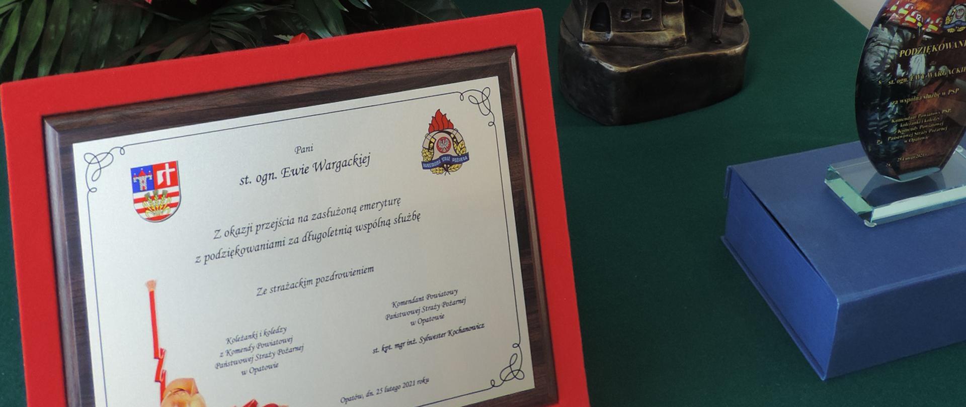 Zdjęcie przedstawia grawerton, kwiaty, rzeźbę św. Floriana oraz pamiątkową statuetkę 