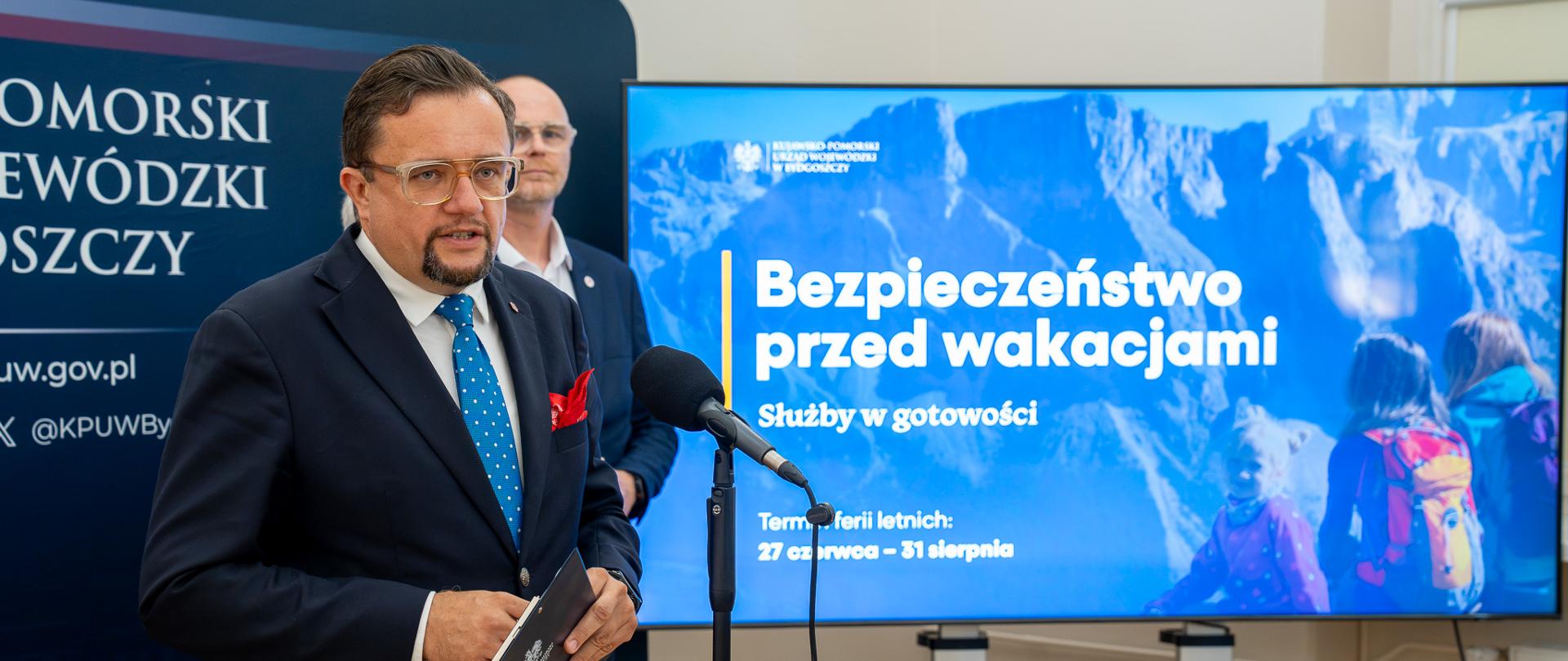 Ireneusz Nitkiewicz oraz Tomasz Okoński, po prawej stronie zdjęcia telewizor z prezentacją: Bezpieczeństwo przed wakacjami 