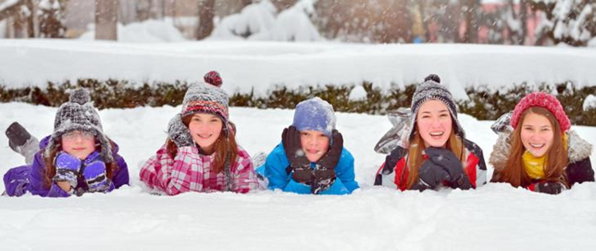 Zdjęcie przedstawia pięcioro dzieci leżących na śniegu.