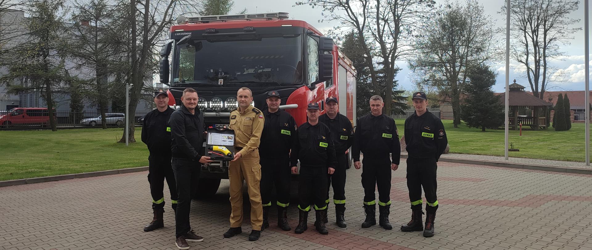 Zdjęcie grupowe na tle samochodu strażackiego w trakcie przekazania nowego sprzętu